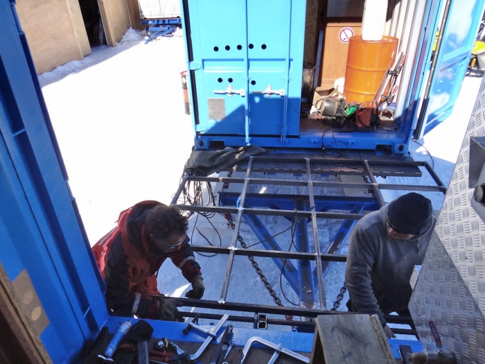A mobile camp made of containers has been installed in Crown Bay for the German team. Kistof and François are installing a module to connect two containers. - International Polar Foundation